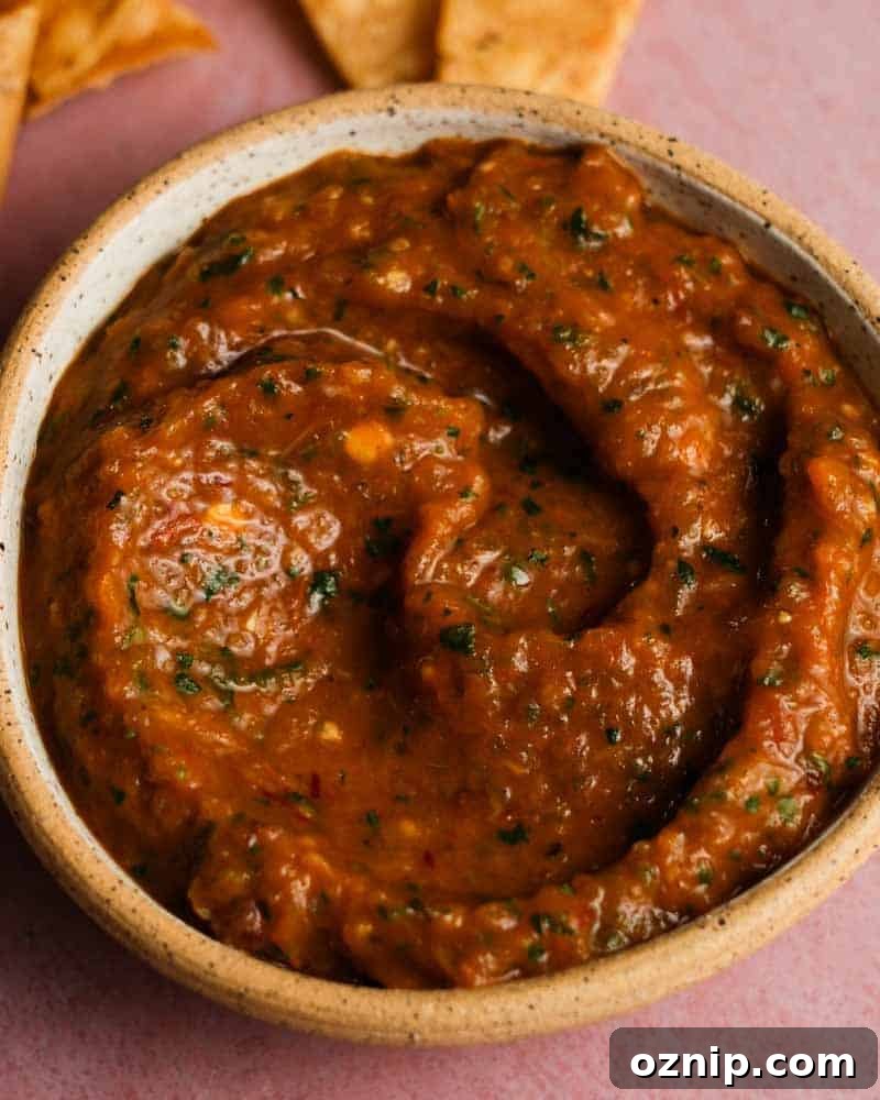 A bowl of roasted chipotle salsa with herbs, beside tortilla chips.