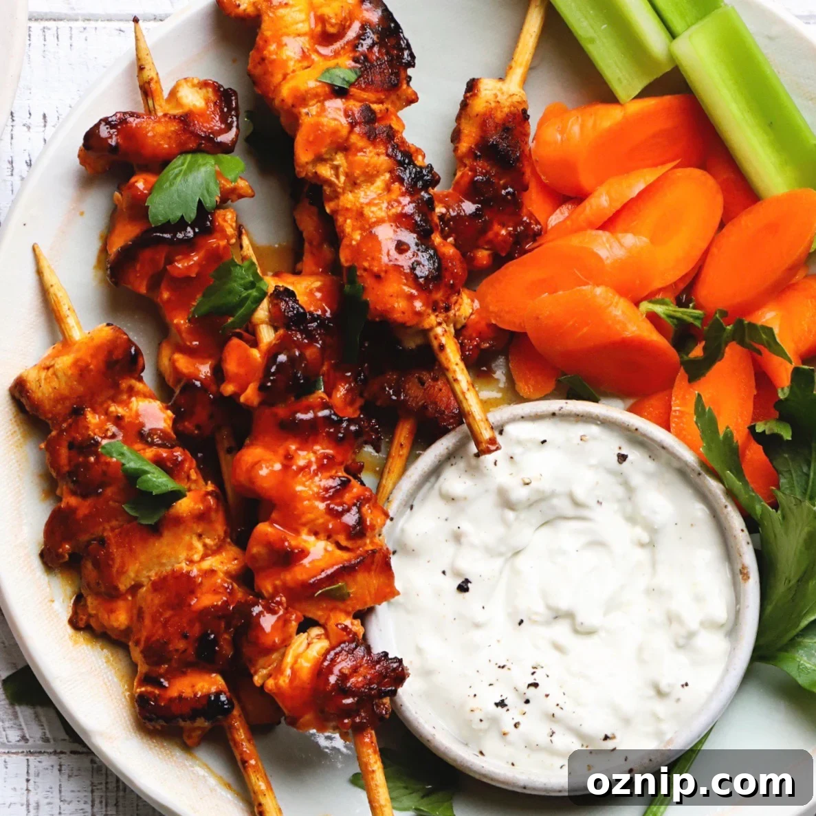 Buffalo chicken skewers with carrot slices, celery, and a bowl of ranch dip.