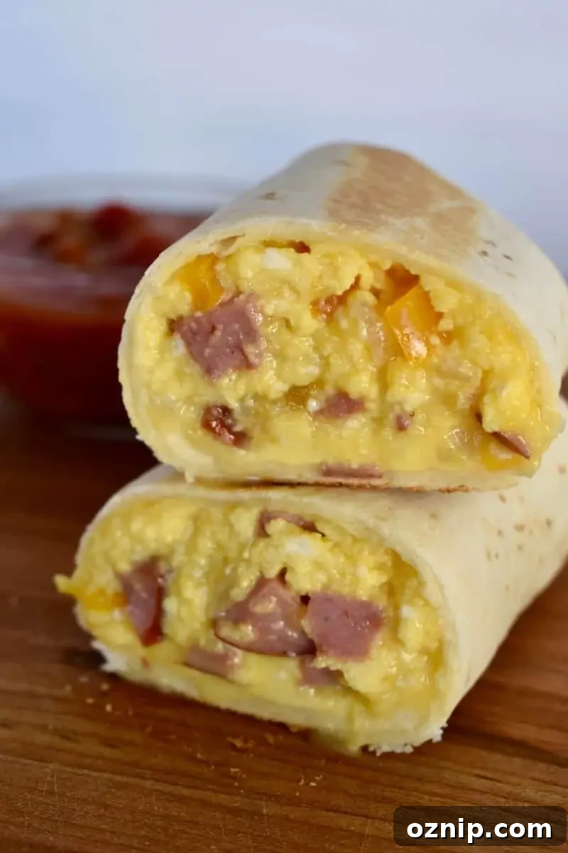 Freezer-Friendly Turkey Sausage Breakfast Burritos Recipe 2 Freezer Breakfast burritos with turkey sausage stacked on each other on a wood cutting board.