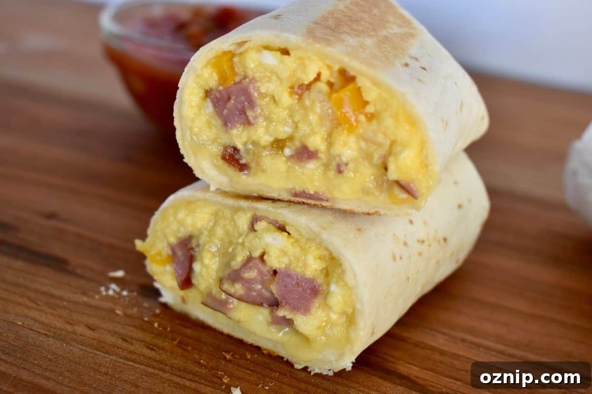 Freezer-Friendly Turkey Sausage Breakfast Burritos Recipe 7 Breakfast burrito with turkey sausage cut in half and stack on each other on wood cutting board.