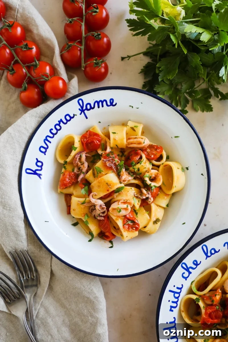 Calamarata Pasta with Calamari in Tomato Sauce Recipe 2 Calamarata pasta with calamari rings and tentacles and blistered tomatoes in a white and blue enamel bowl.