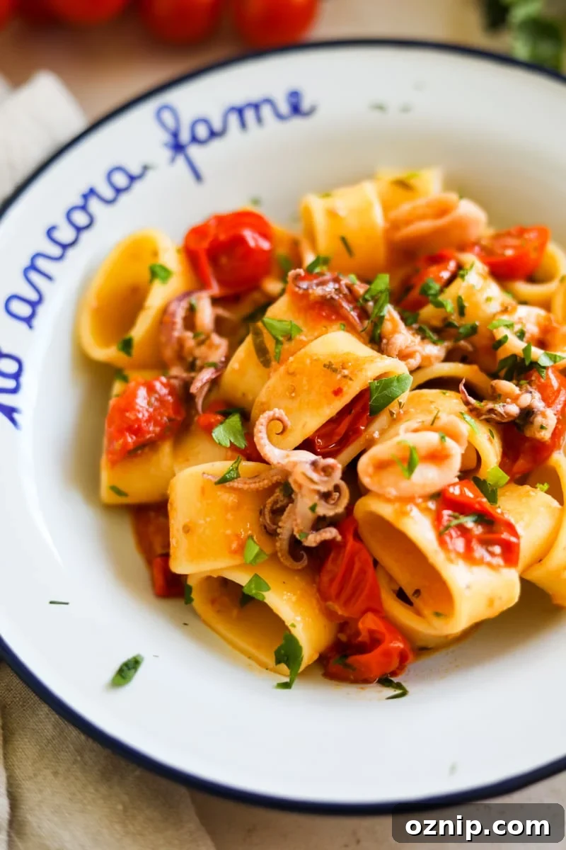 Calamarata Pasta with Calamari in Tomato Sauce Recipe 5 Closeup shot of Calamarata calamari and tomato pasta in a white bowl.