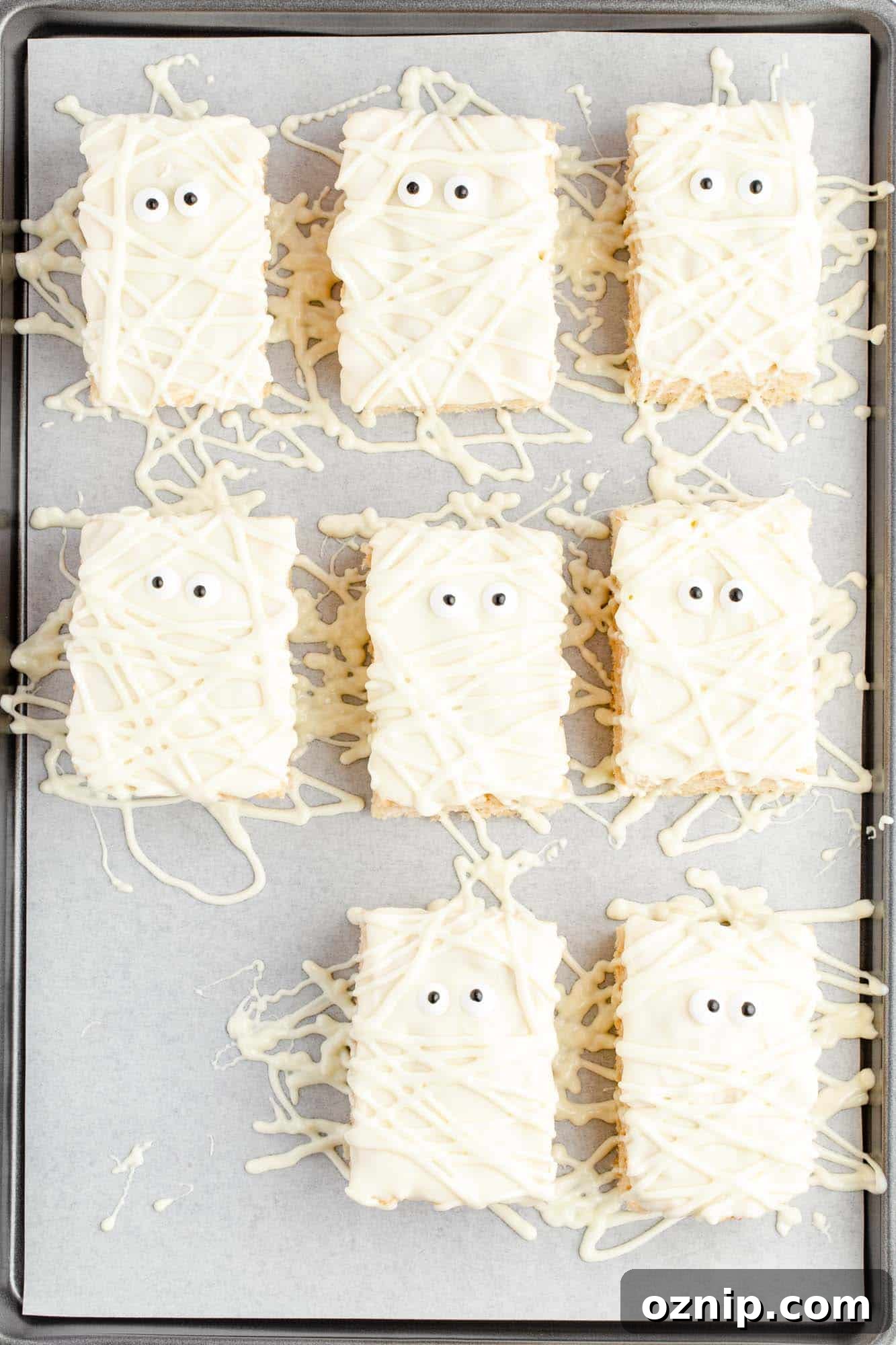 Overhead shot of rice krispie treats that are decorated to look like mummies, placed on a cookie sheet lined with parchment paper.