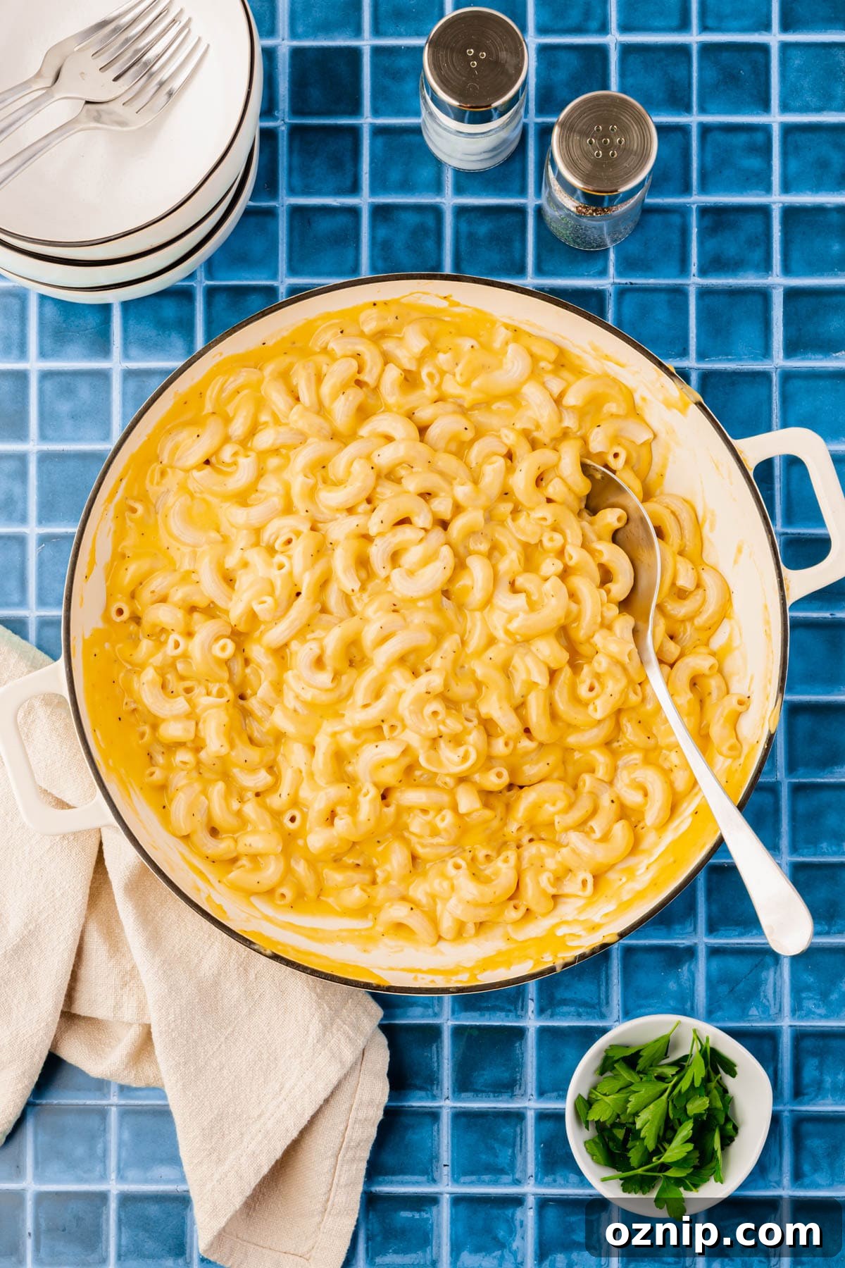 A table set with a large pot of gluten-free mac and cheese, salt and pepper, and fresh parsley.