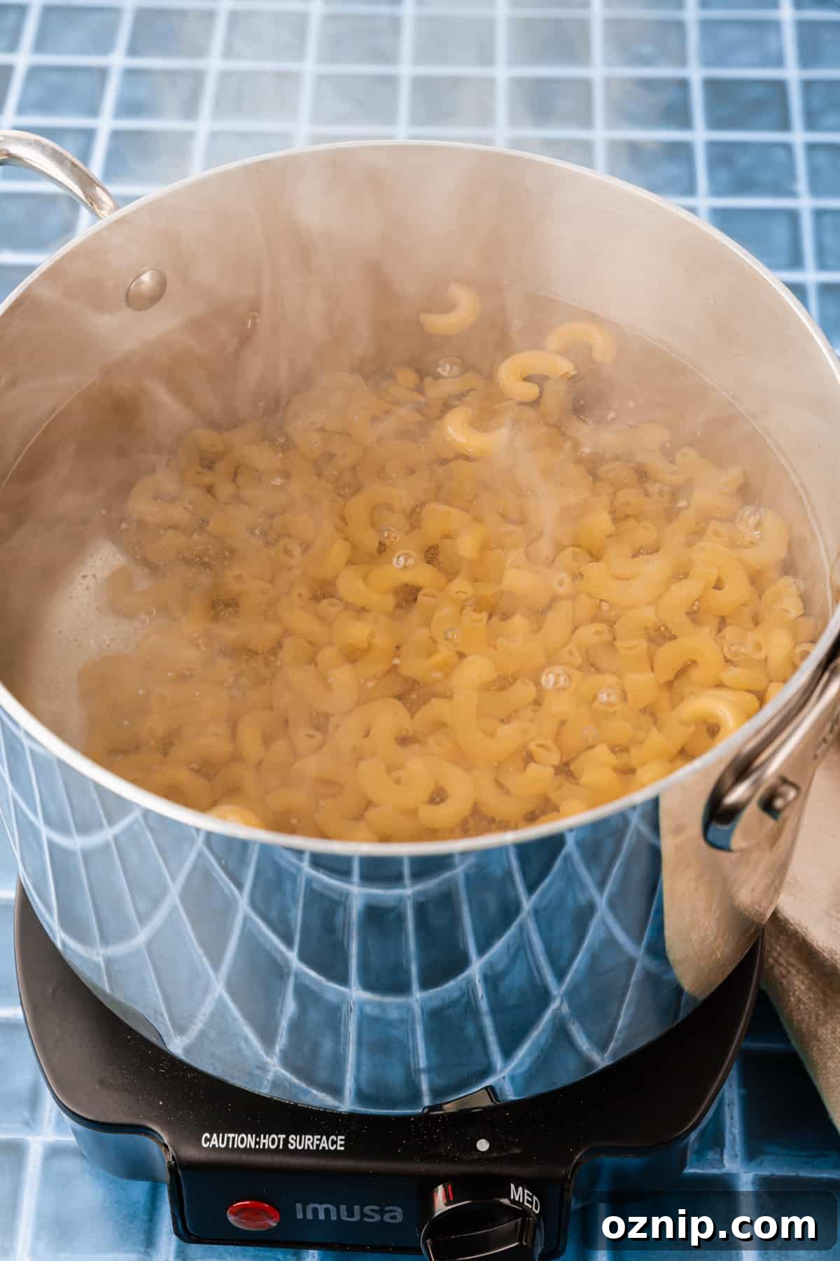 Creamy Gluten Free Mac and Cheese Recipe 4 A stainless steel pot of water cooking gluten free macaroni noodles on a hot plate.