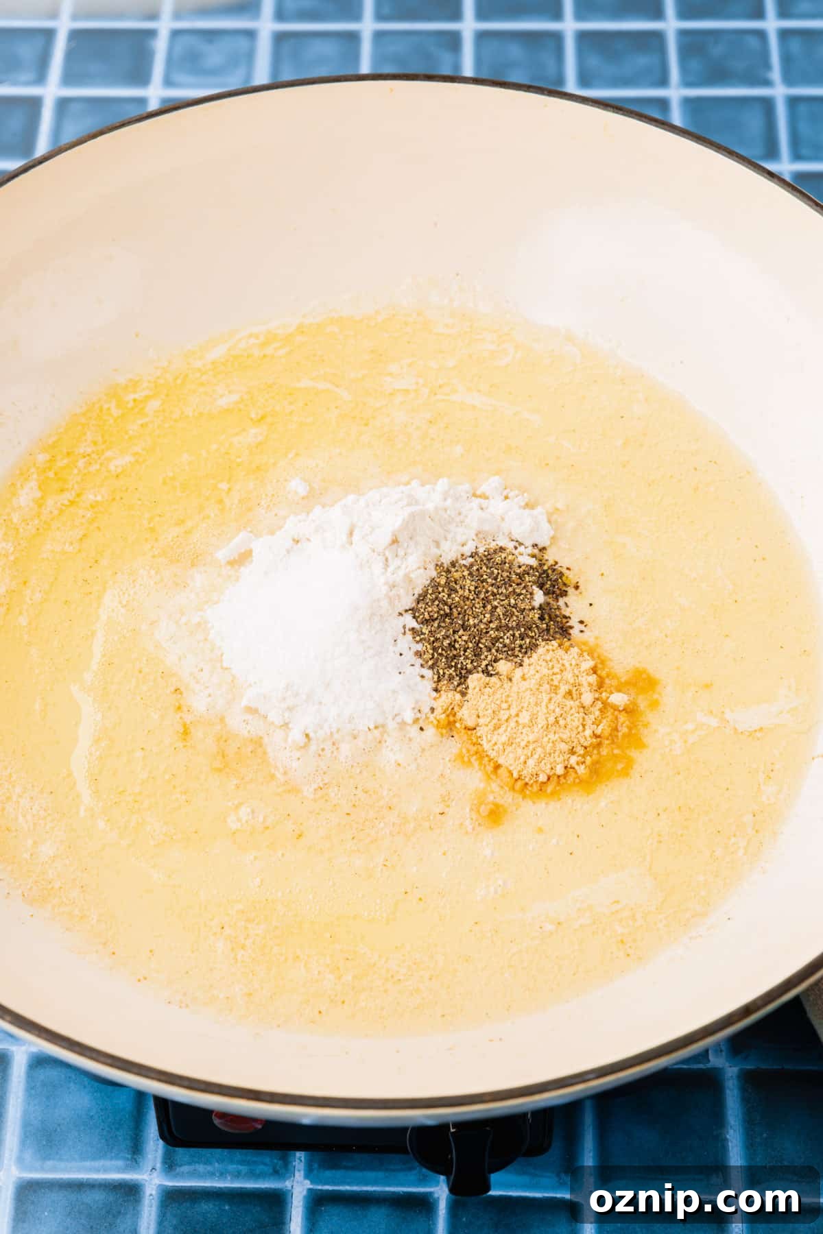 Creamy Gluten Free Mac and Cheese Recipe 5 A white braising pan with melted butter, gluten-free flour, ground mustard powder and black pepper before mixing together to make a roux.
