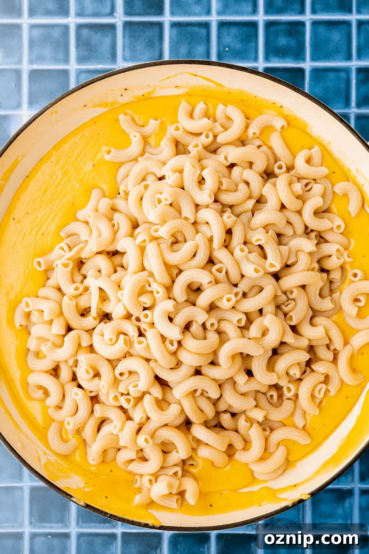 Creamy Gluten Free Mac and Cheese Recipe 10 An overhead view of a skillet of gluten free macaroni pasta on top of a gluten-free cheese sauce before mixing together.