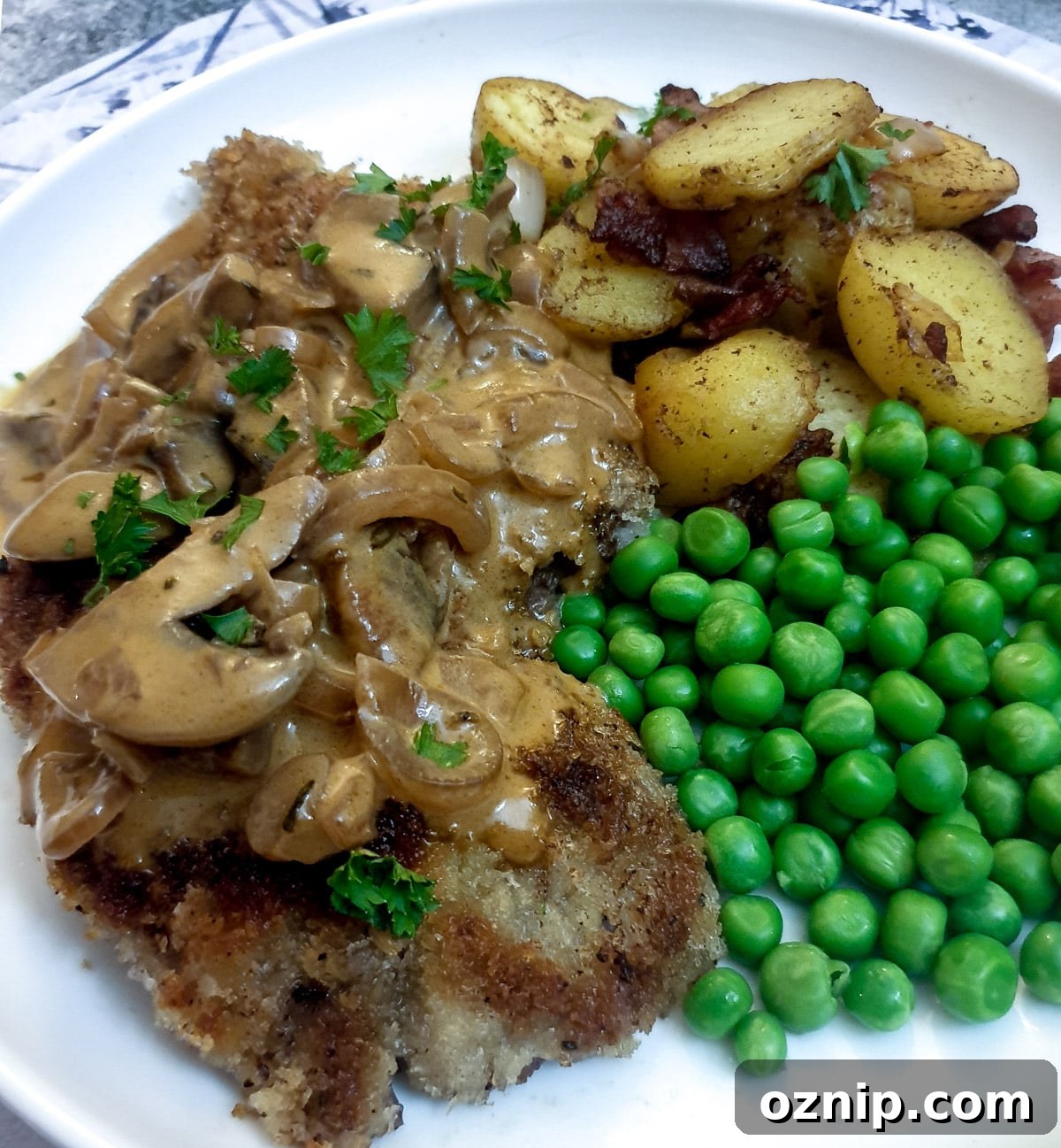 A crispy crumbed beef schnitzel on a plate with potatoes, peas and a mushroom sauce.