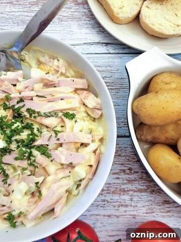 A dish of German meat salad next to a bowl of potatoes and some crusty bread.