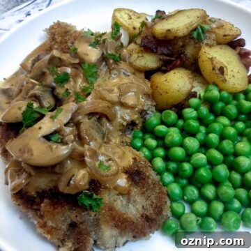 A crispy crumbed beef schnitzel on a plate with potatoes, peas and a mushroom sauce.