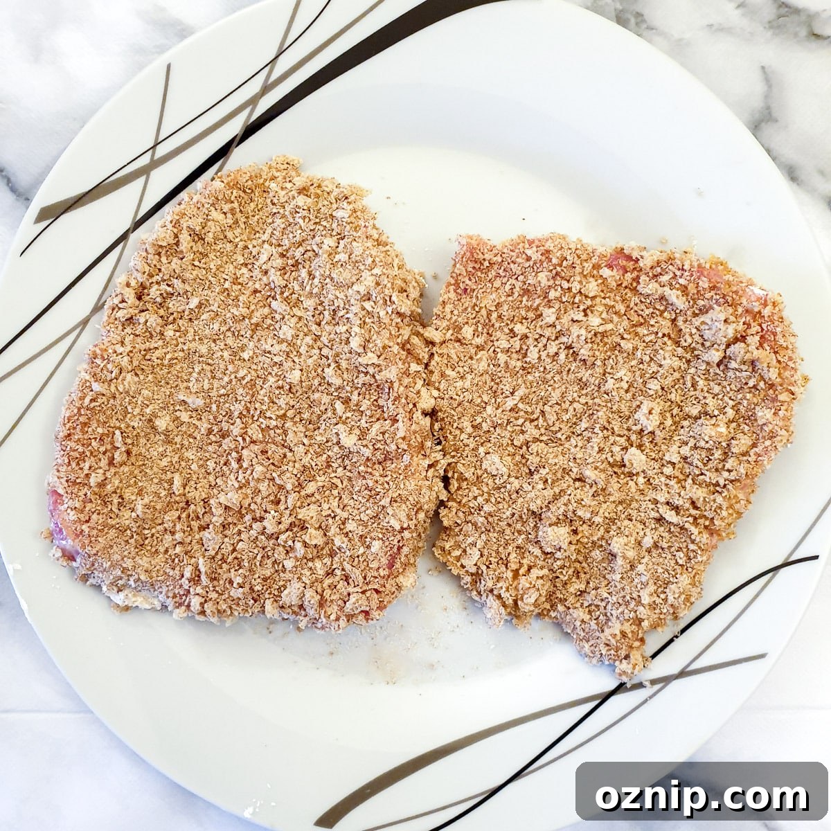 2 coated schnitzels on a plate, ready for frying.