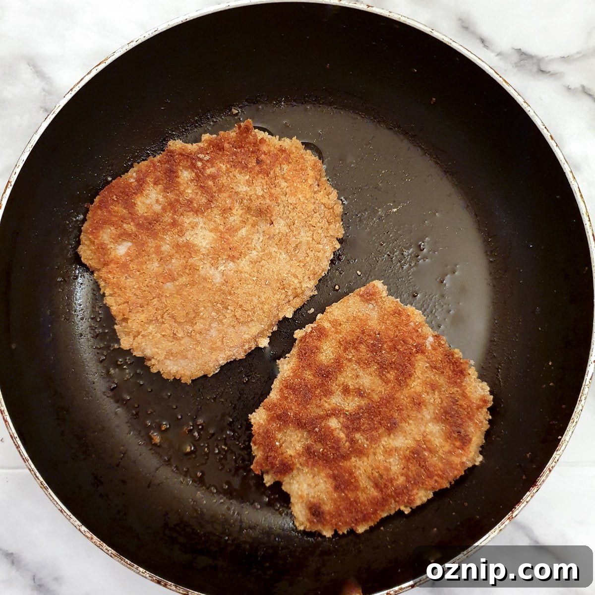 2 schnitzels browning in a frying pan.