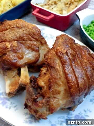 Two crispy-skinned eisbein on a plate next to a selection of vegetables.