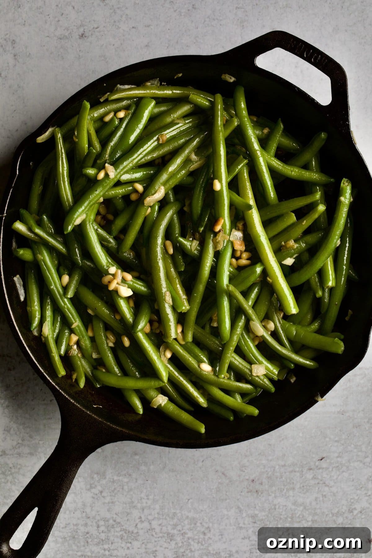 process of making sautéed green beans: mixing green beans with onions and pine nuts in iron skillet pan