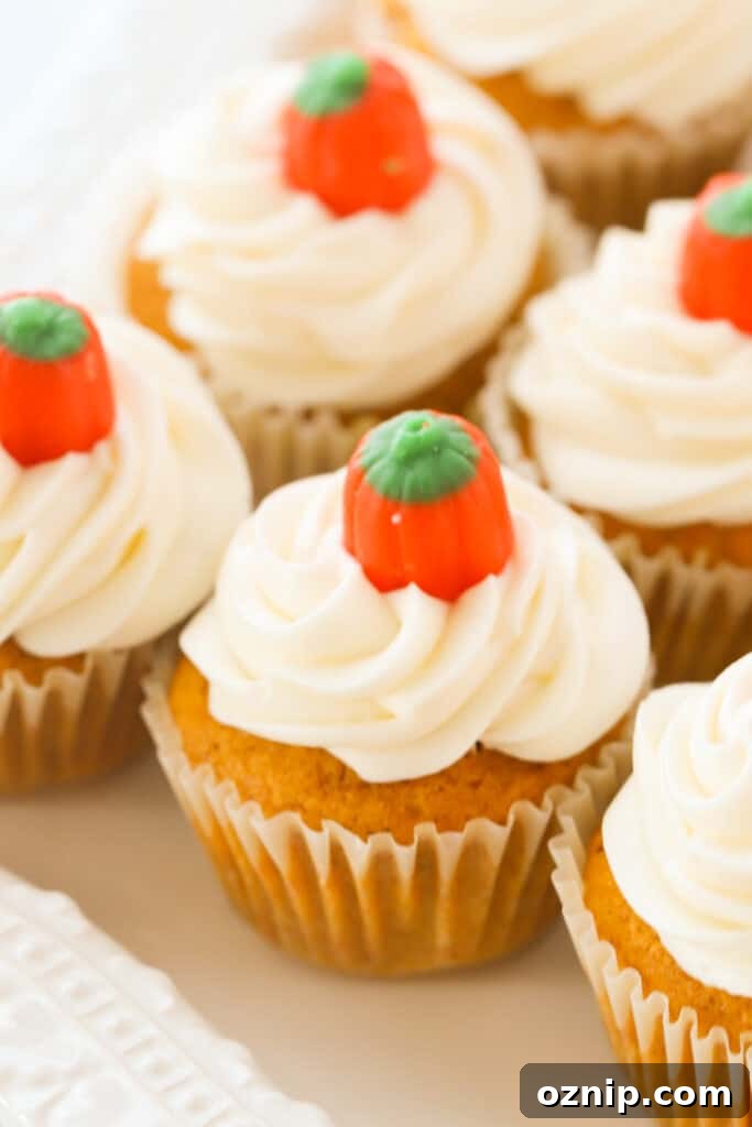 Cream cheese frosted pumpkin cupcakes lined up on a table and garnished with little candy pumpkins.