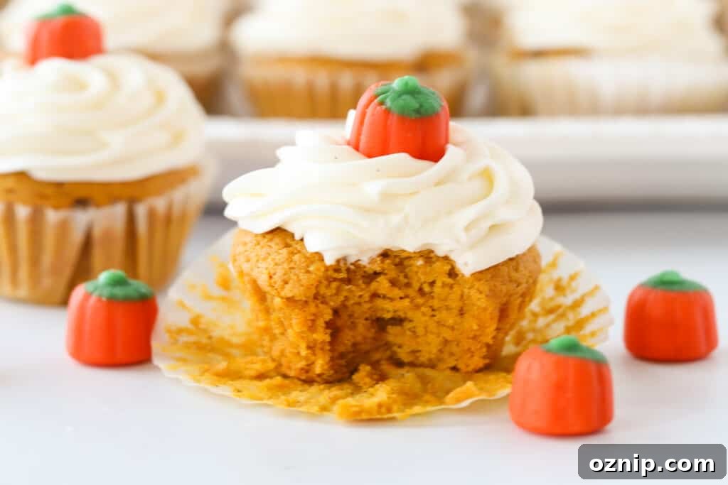 A pumpkin cupcake, topped with frosting and a candy pumpkin, with a bite taken out of it.