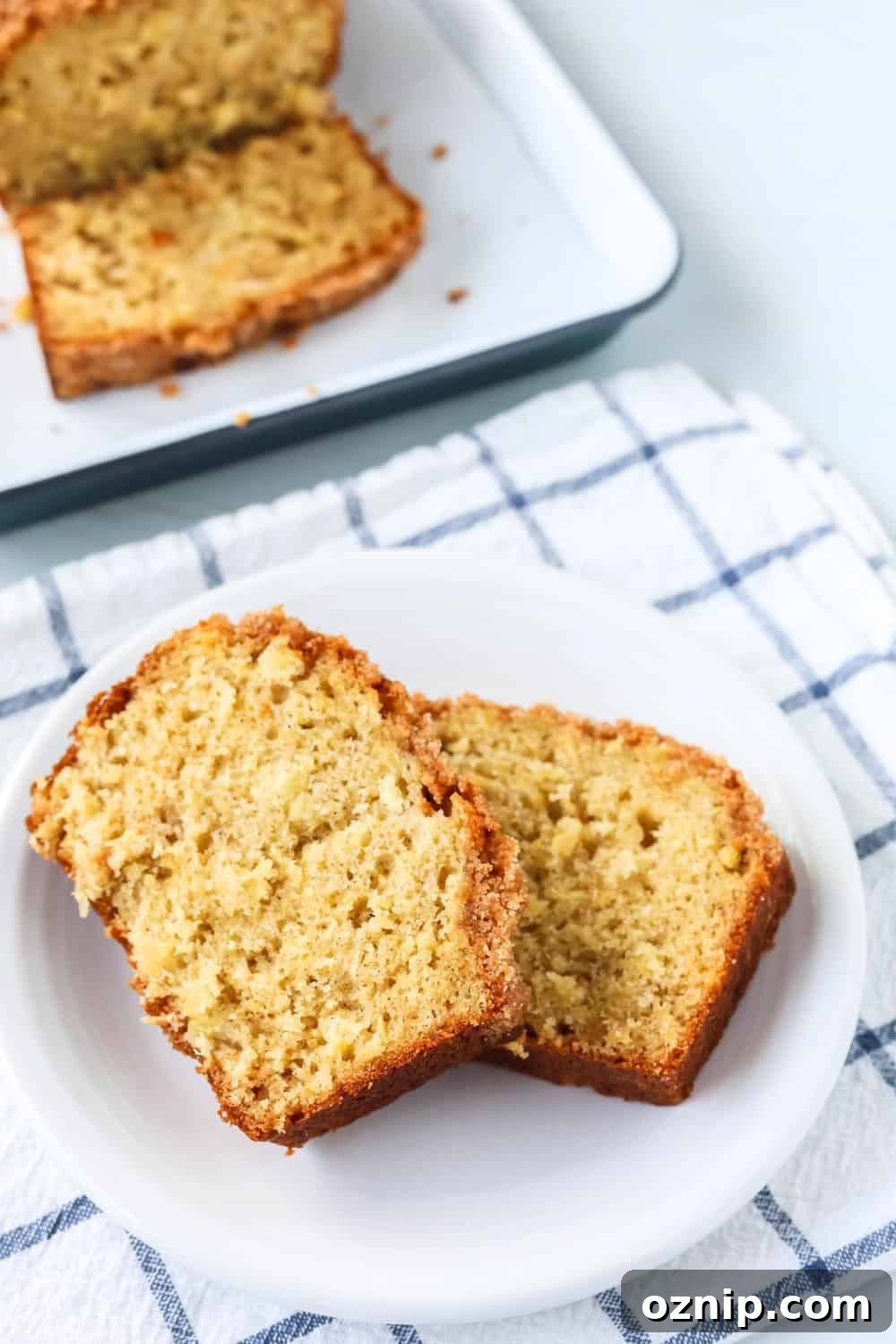 two slices of sweet pineapple bread are served on a white plate. The remainder of the loaf of quickbread is in the background.