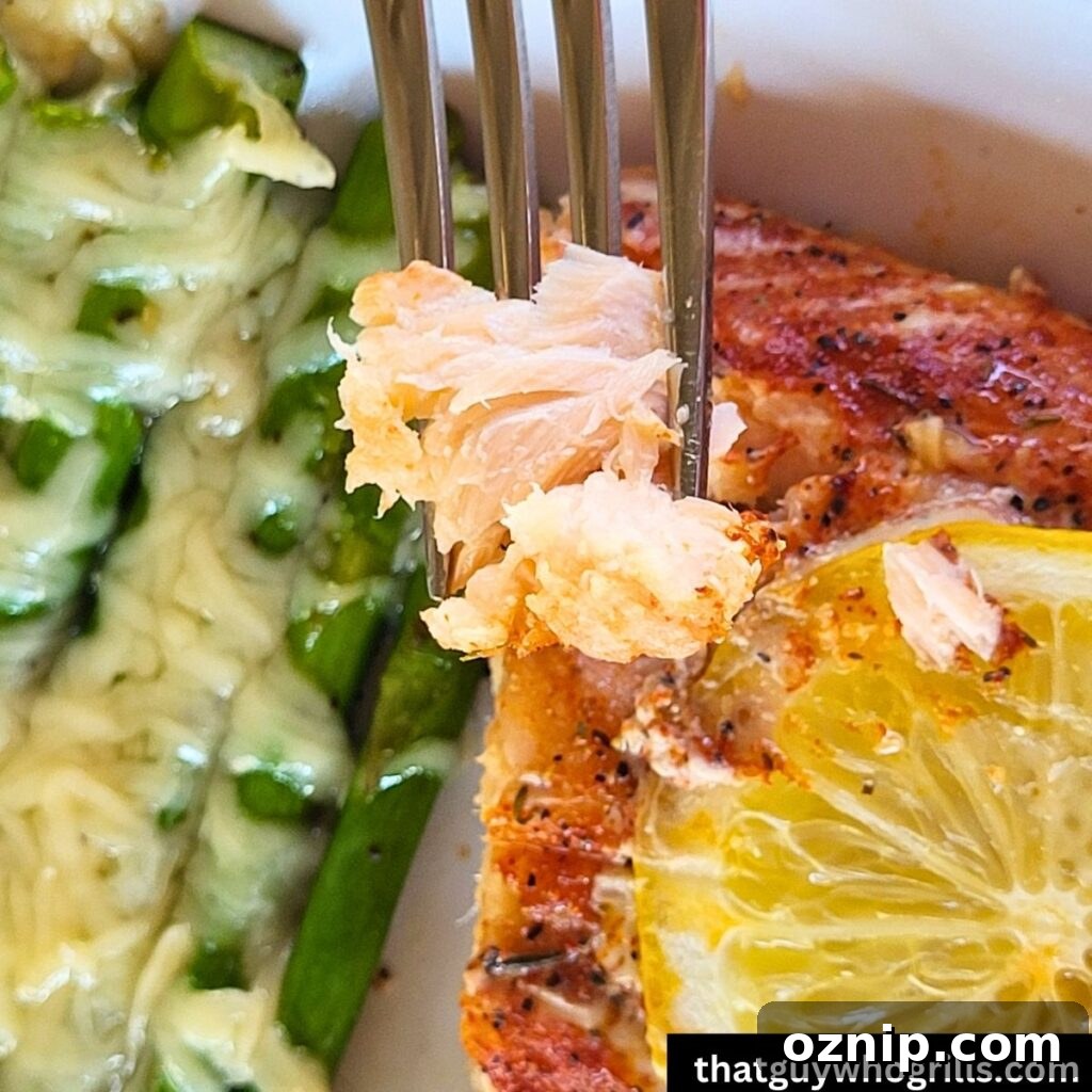 Salmon on a fork over a salmon fillet by cheesy asparagus