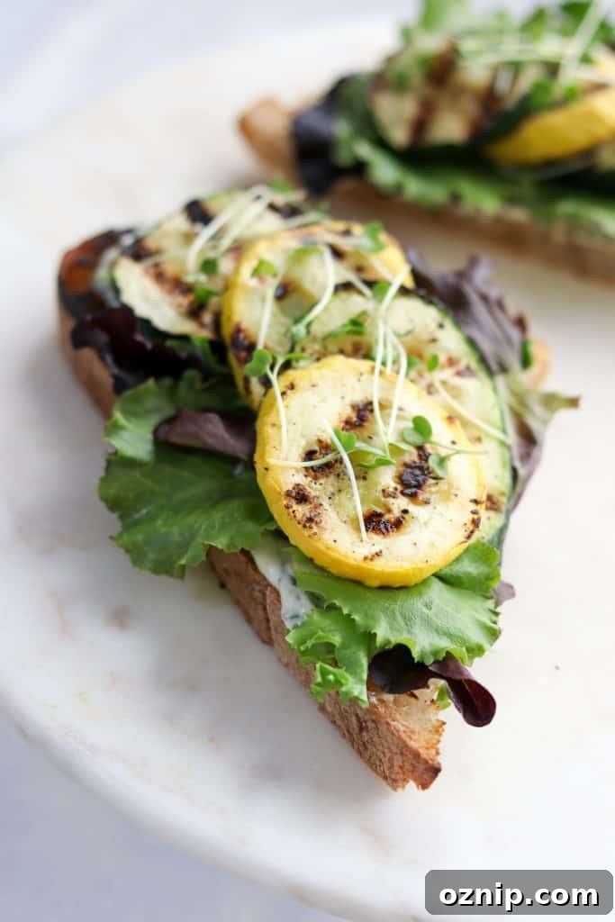 A close up of an open sandwich with grilled summer squash and lettuce