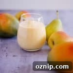 Glass of pear mango smoothie with mangoes and pears in background