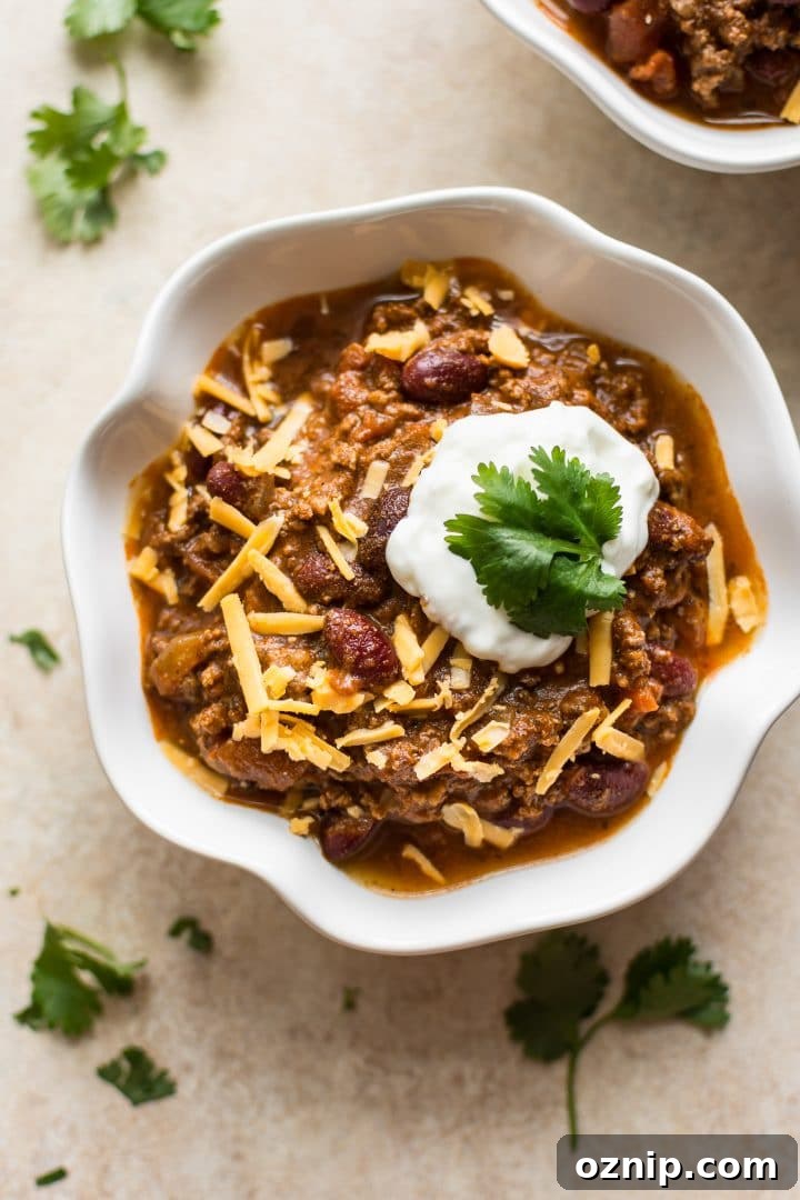 white bowl with electric pressure cooker beef chili topped with sour cream, cheese, and cilantro