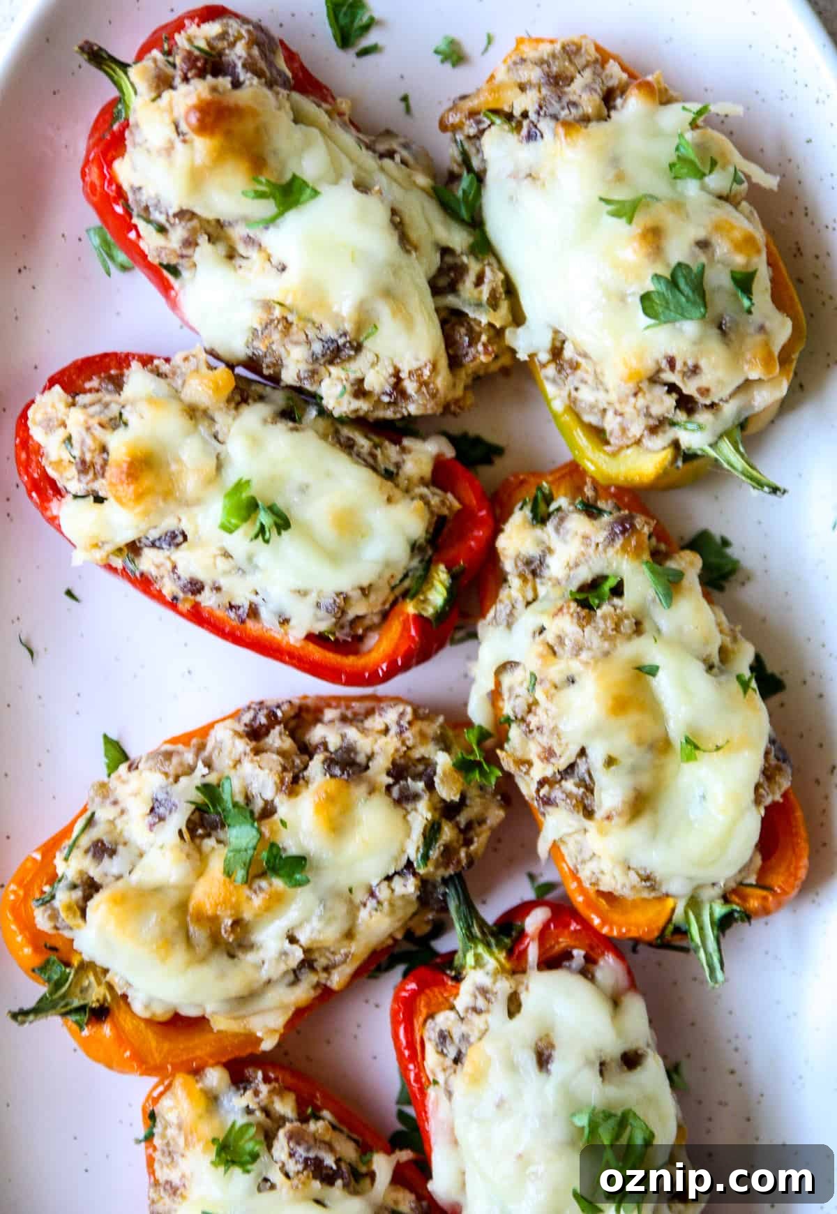 Sausage Stuffed Mini Peppers Recipe 2 Multi colored sausage stuffed mini peppers on a white plate.