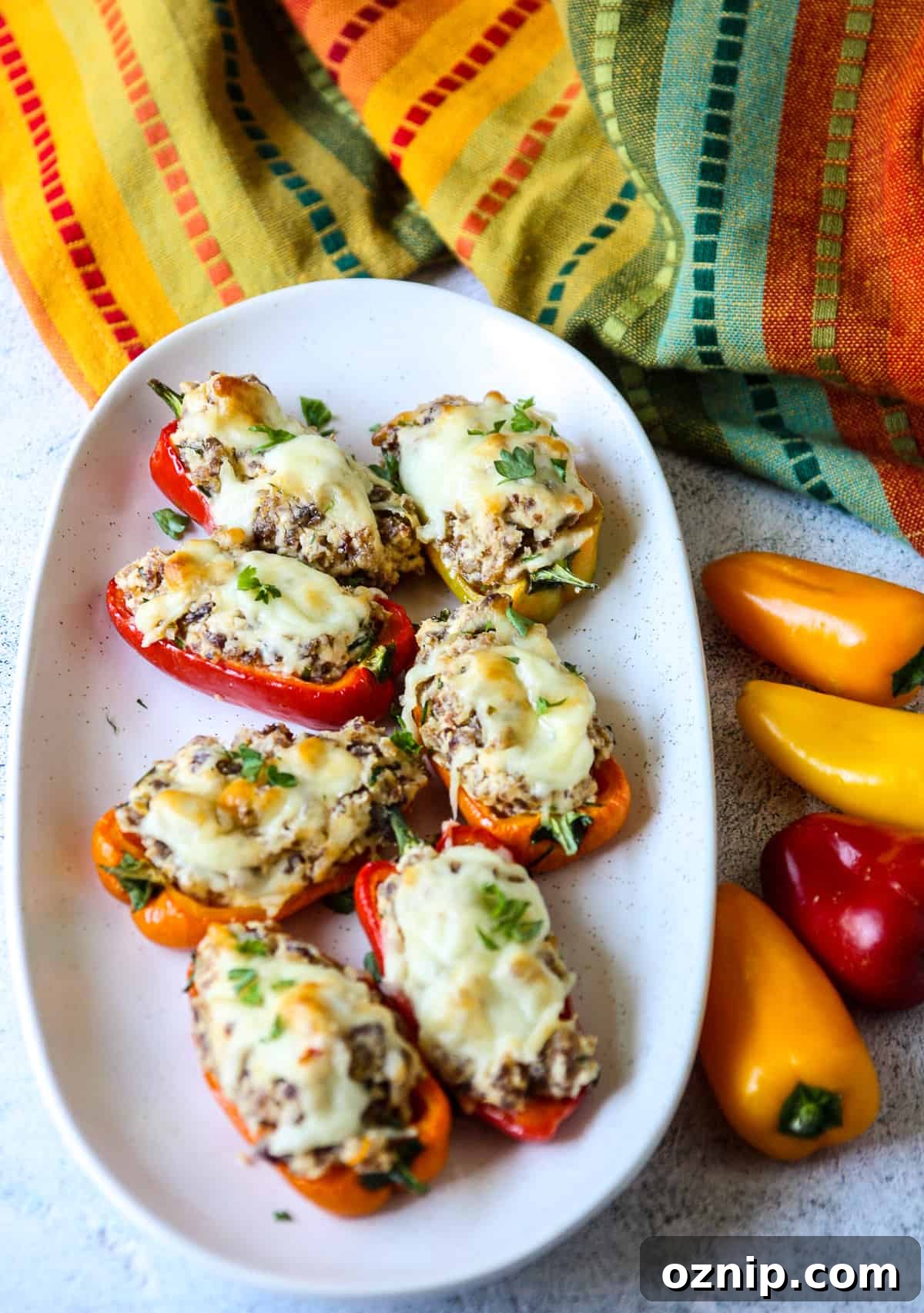 Sausage Stuffed Mini Peppers Recipe 3 Sausage stuffed mini peppers on a serving platter, beside some fresh whole mini peppers.