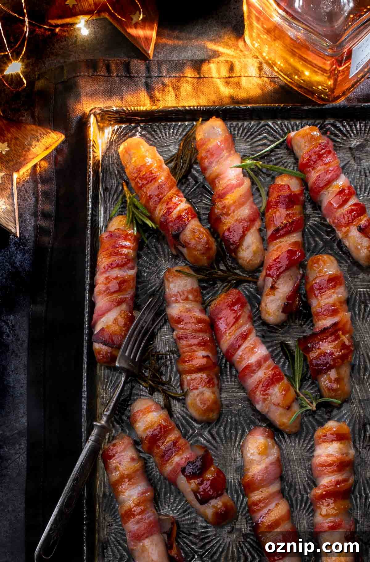Whiskey Honey Glazed Pigs in Blankets 2 Cooked pigs in blankets on a baking tray next to a bottle of whiskey.