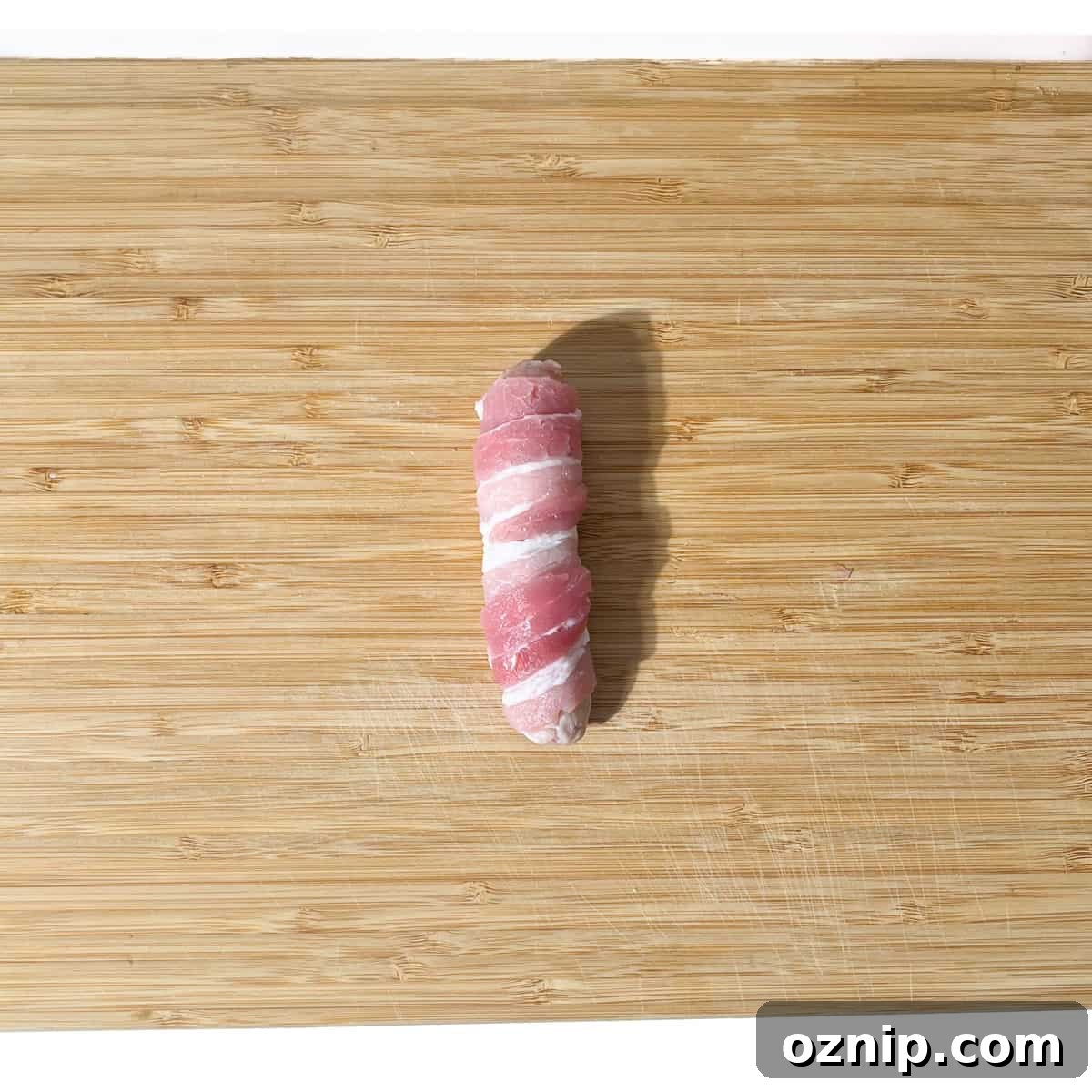 Whiskey Honey Glazed Pigs in Blankets 11 A completed rolled pig in blanket on a chopping board.
