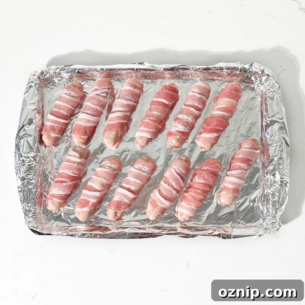 Whiskey Honey Glazed Pigs in Blankets 12 Pigs in blankets on a baking tray, spaced out.