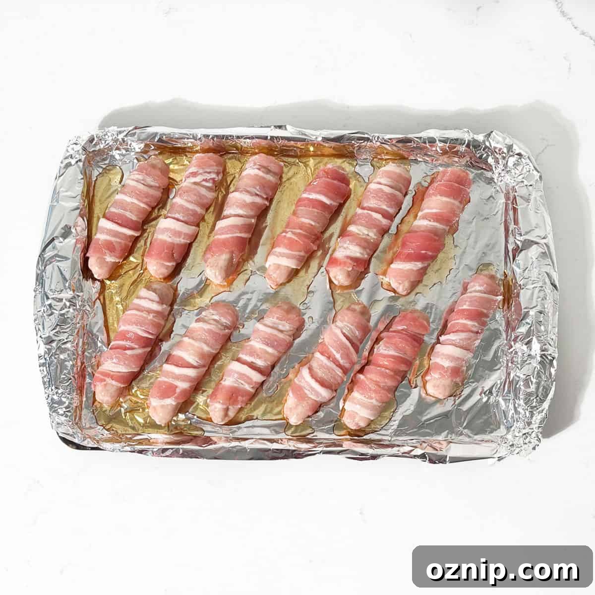 Whiskey Honey Glazed Pigs in Blankets 13 Pigs in blankets on a baking tray with the glaze drizzled over.