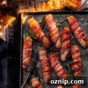 Whiskey Honey Glazed Pigs in Blankets 15 Cooked pigs in blankets on a baking tray next to a bottle of whiskey.
