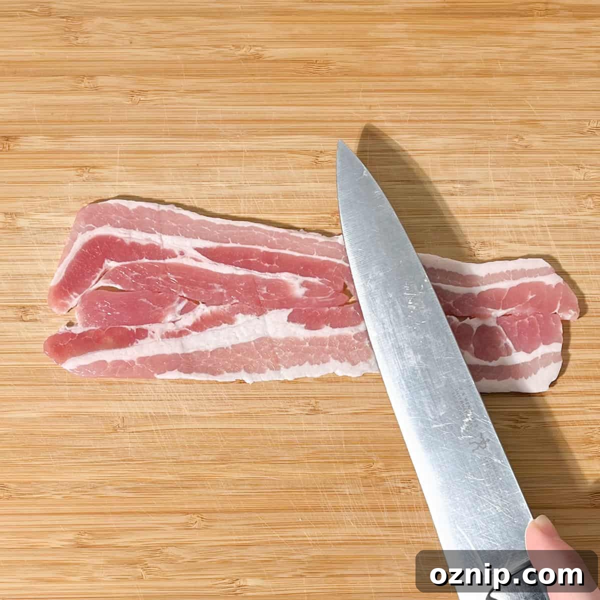 Whiskey Honey Glazed Pigs in Blankets 7 Stretching a piece of bacon with a large knife.
