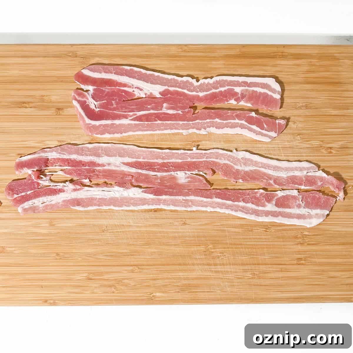 Whiskey Honey Glazed Pigs in Blankets 8 Two pieces of bacon on a chopping board, one stretched and one unstretched.