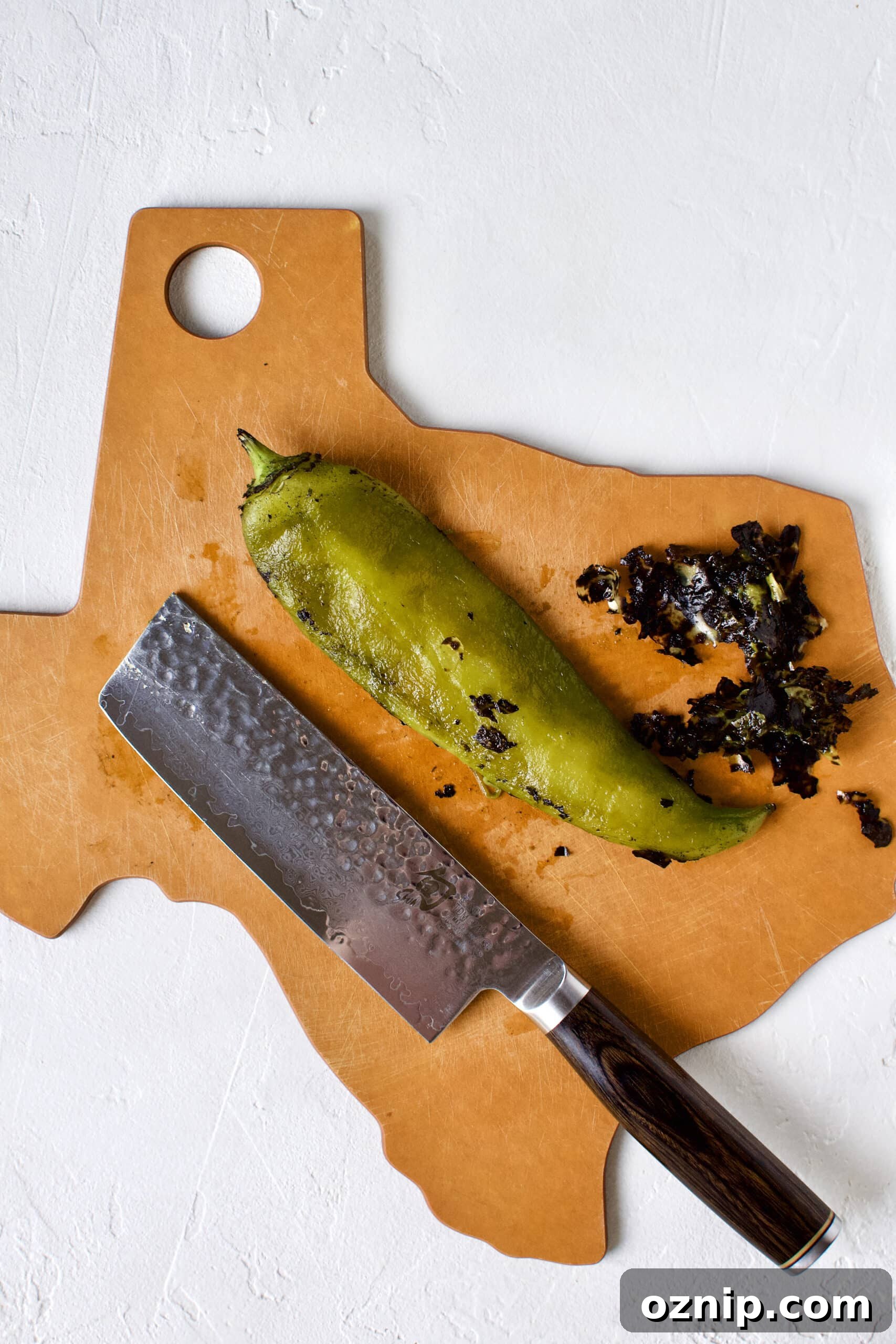 Cleaning a hatch chile by removing the charred skin with the back of a knife.