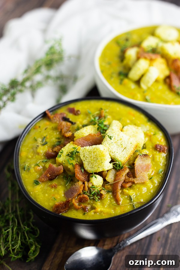Split pea soup in a black matte bowl topped with bacon, croutons, and thyme leaves with a second bowl behind.