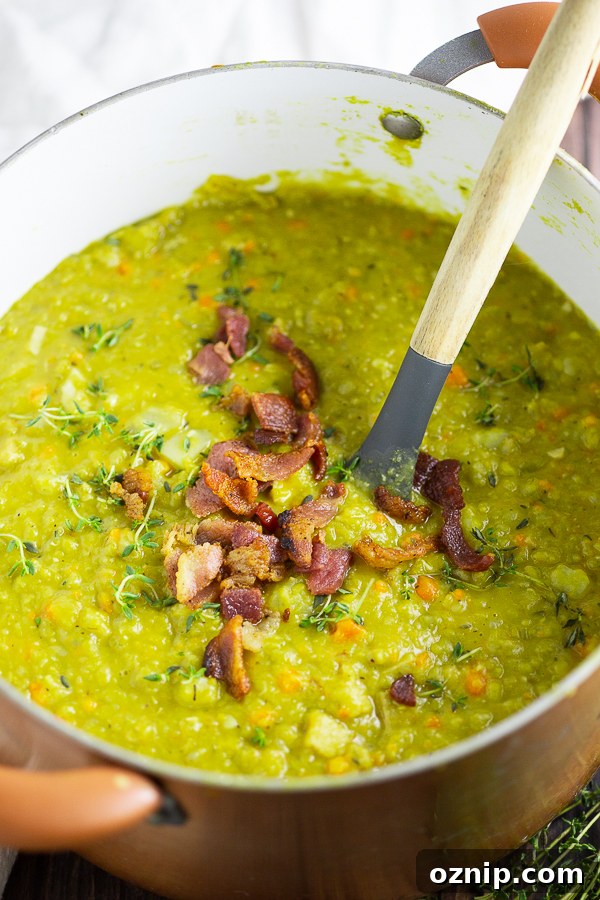 Split pea soup in a copper pot topped with bacon with a wooden spoon in the middle