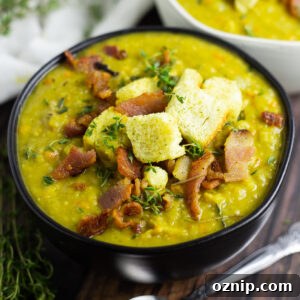 Split pea soup in a matte black bowl topped with crumbled bacon, fresh thyme, and croutons.