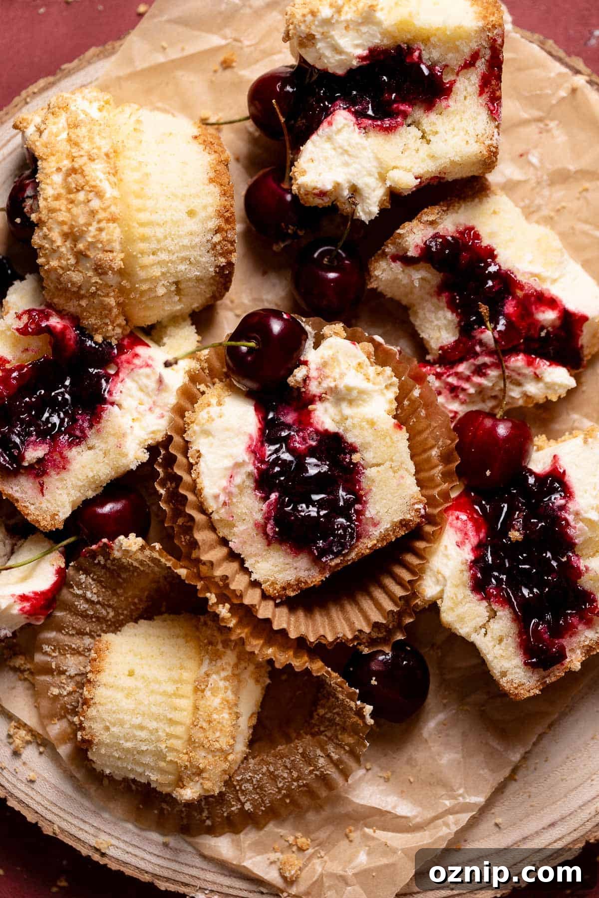 Cherry Cheesecake Cupcakes with Graham Cracker Crust 2 Cherry cheesecake cupcakes cut in half on a piece of parchment paper.