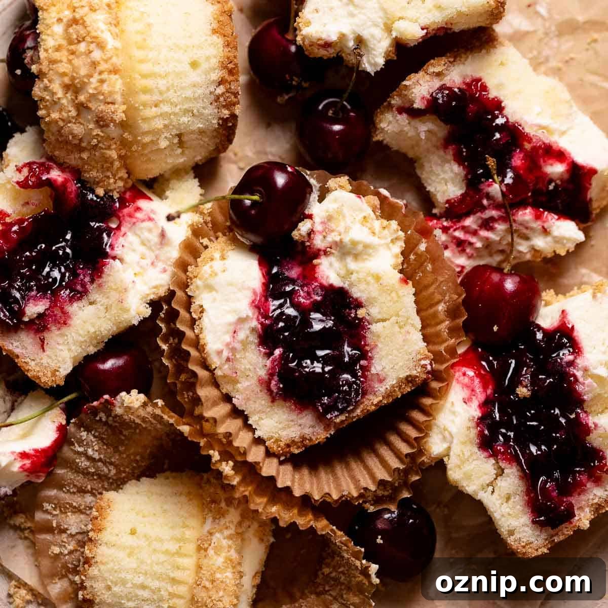 Cherry Cheesecake Cupcakes with Graham Cracker Crust 7 Cherry cheesecake cupcakes cut in half on brown parchment paper.