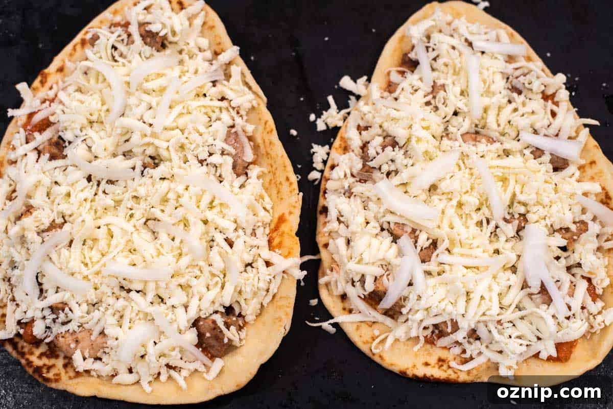 Naan topped with sauce, chicken and cheese on baking sheet.