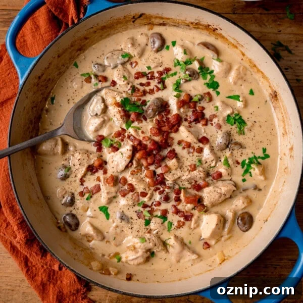 A blue cast iron pan filled with chicken in a cream-cider sauce, topped with crispy bacon and parsley.