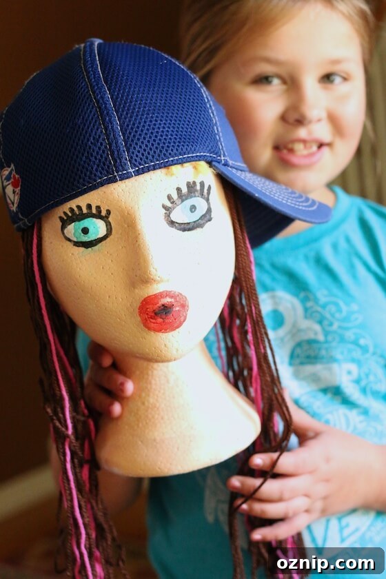 Styrofoam Head Self Portrait Art Project for Kids 3 girl holding styrofoam head decorated and wearing ball cap