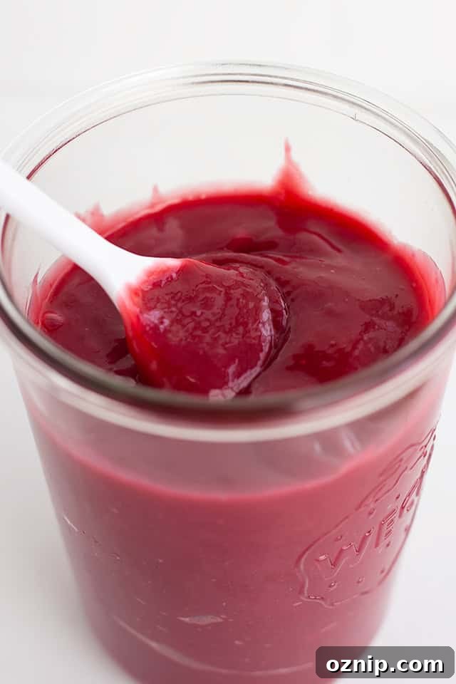 Mixed Berry Curd Recipe 3 A glass jar filled with thick, deep red Mixed Berry Curd, with a white spoon partially submerged in the luscious mixture.