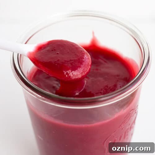 Mixed Berry Curd Recipe 5 A jar filled with smooth, dark red homemade fruit curd, with a white spoon holding a spoonful above the jar.