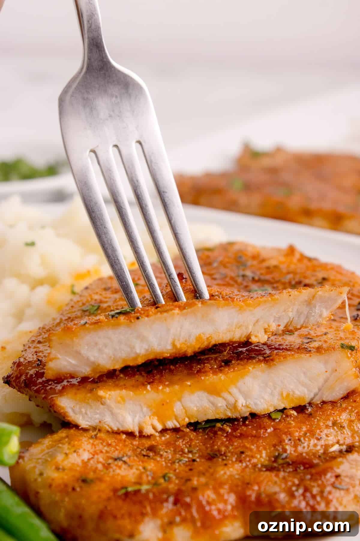Close-up of a juicy air-fried pork chop sliced to reveal the tender inside, served with a fork.
