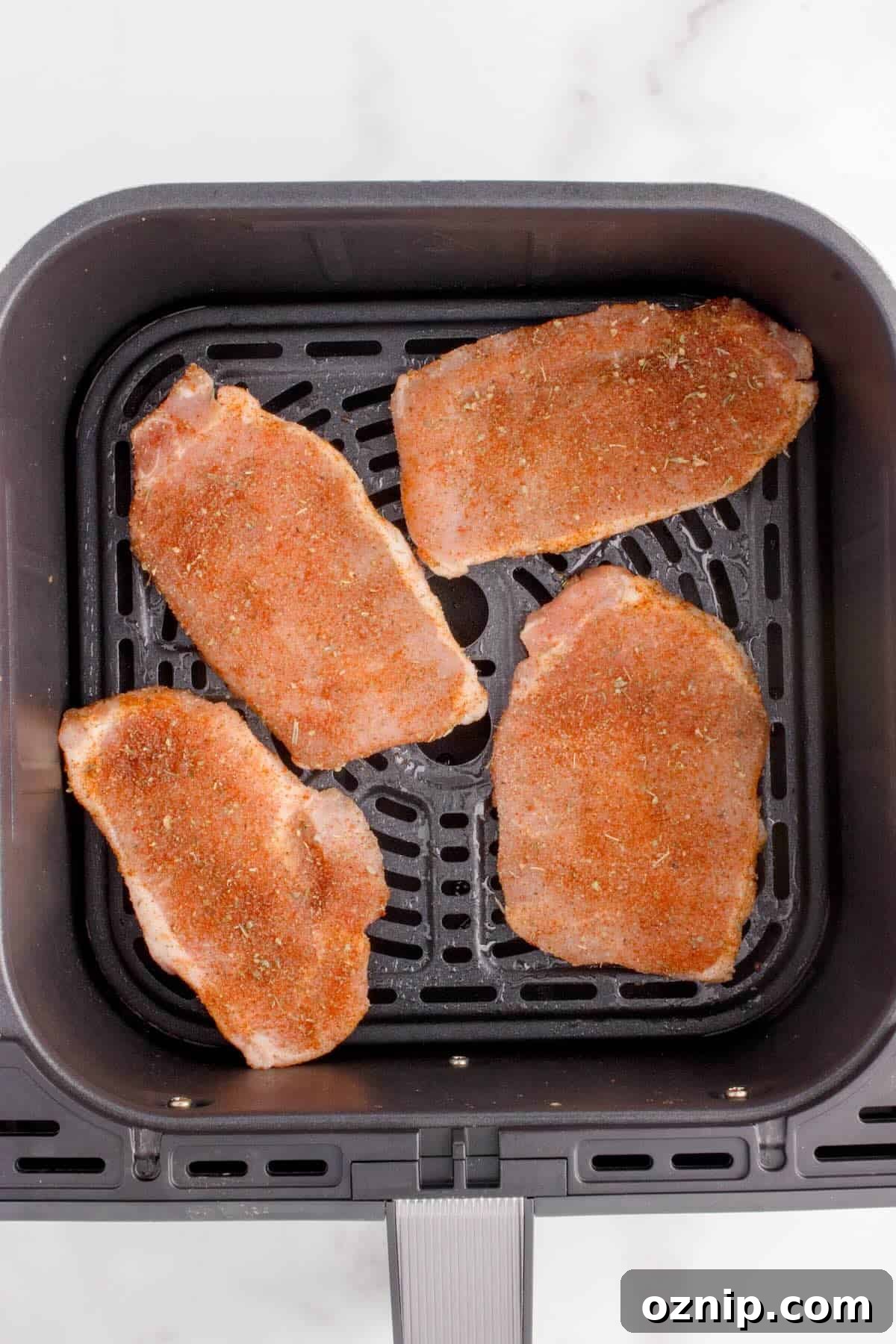 Thin pork chops arranged in a single layer in the air fryer basket.
