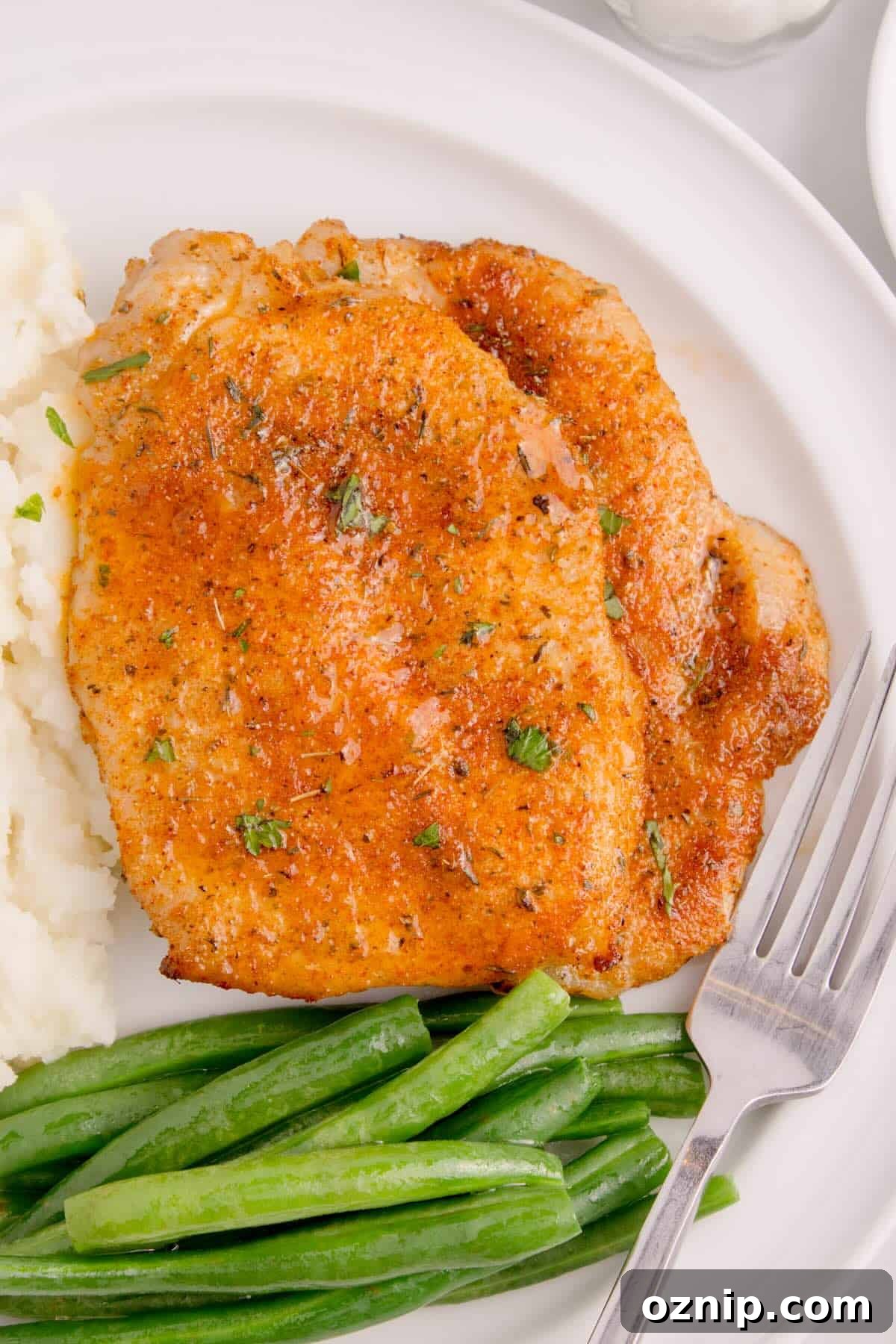 Golden-brown thin pork chops cooked in the air fryer, served on a plate with mashed potatoes and green beans.