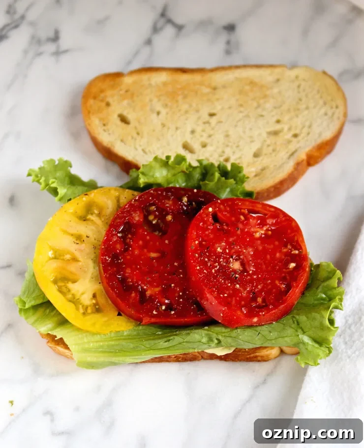 Open faced start of BLT with tomato and lettuce.