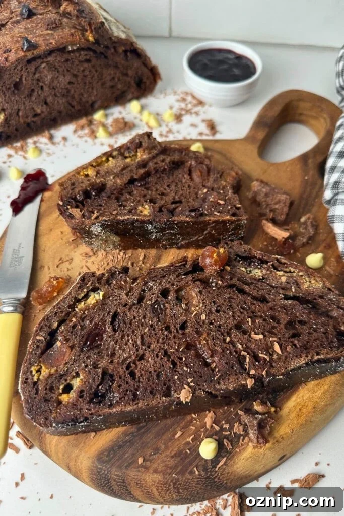 Two slices of sourdough chocolate cherry bread laid out on a wooden serving board. You can see the rest of the loaf in the background.